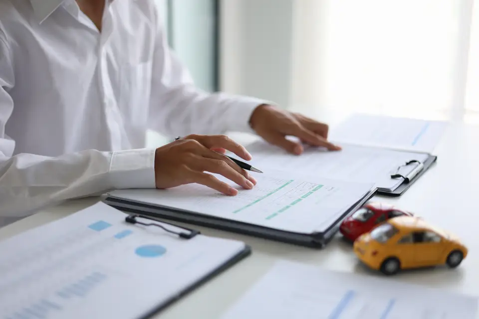 Person in a white shirt reviewing documents on a clipboard at a bright desk, with a yellow toy car nearby.